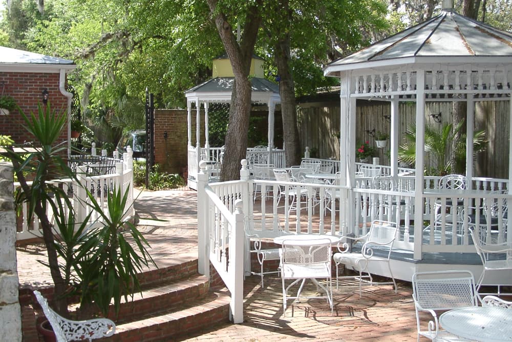 A serene outdoor patio with white wrought iron furniture and gazebos surrounded by greenery.