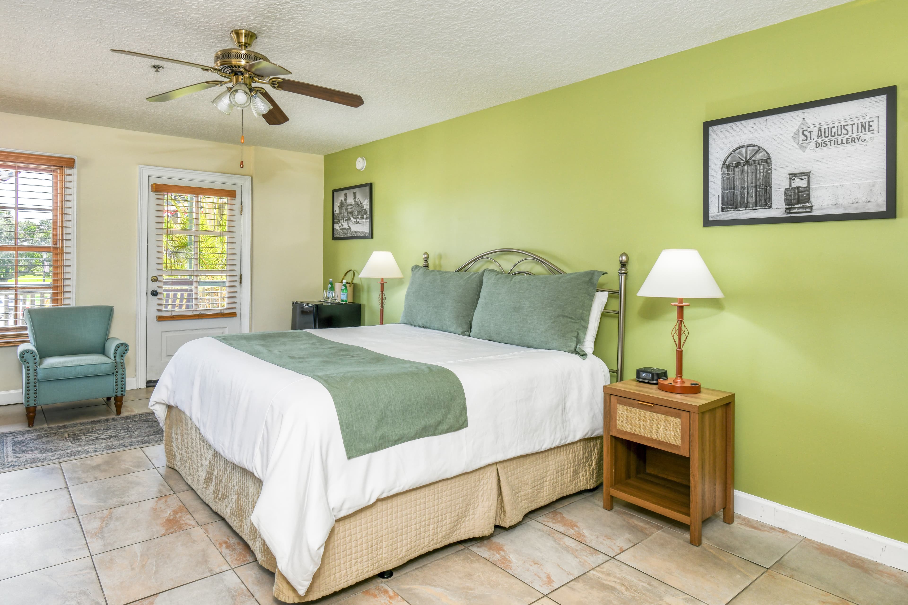 A neatly arranged bedroom featuring a queen bed, green walls, a ceiling fan, and natural light from windows.