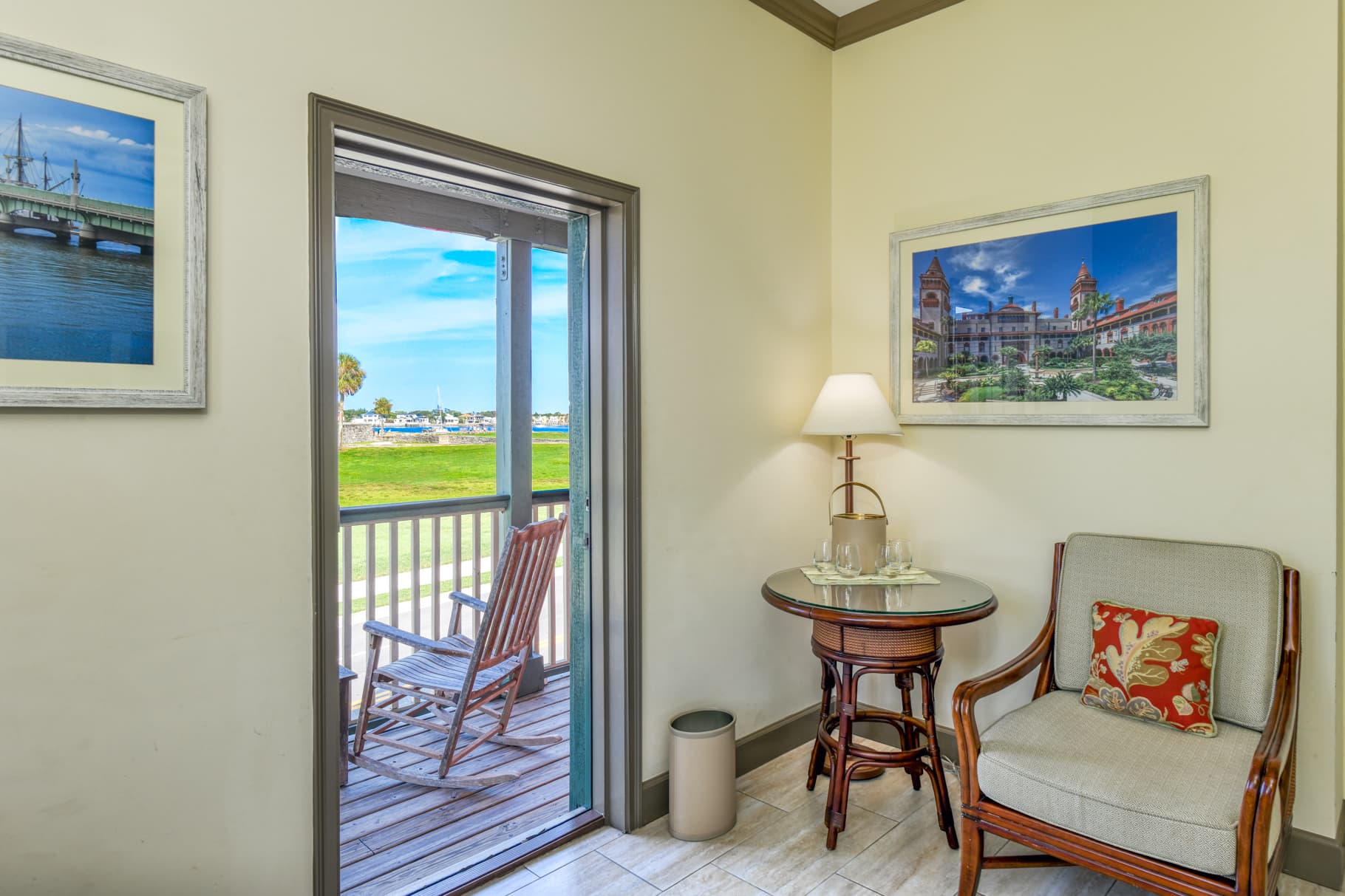 A cozy corner of a room featuring a chair, table with a lamp, and an open door leading to a scenic outdoor view.