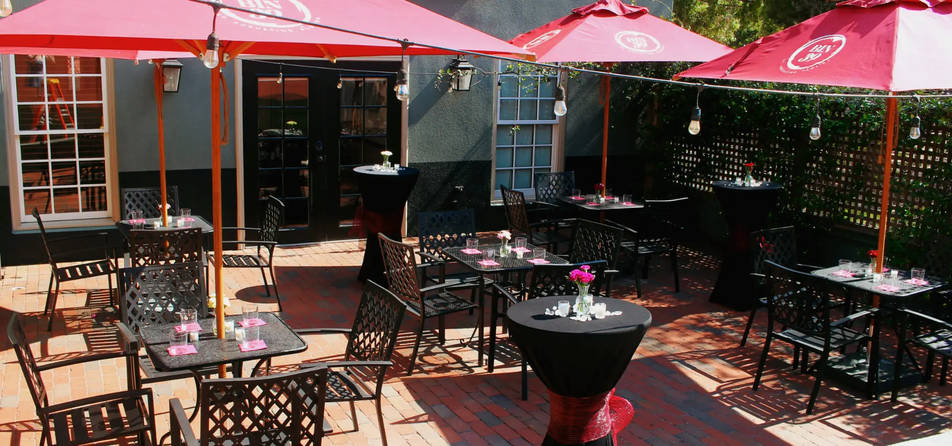 Outdoor dining area with black tables, red umbrellas, and floral centerpieces.